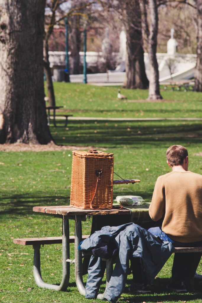 A couple enjoys a sunny picnic in a lush park, seated on a wooden bench with a wicker basket.